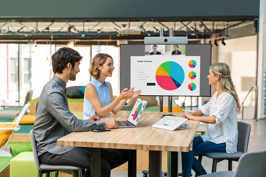 Three people sitting around a desk during a cisco webex meeting with a cisco webex device for corporate collaboration solutions