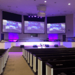 Church worship center stage with lighting and screens displaying the MCC Church technology solutions