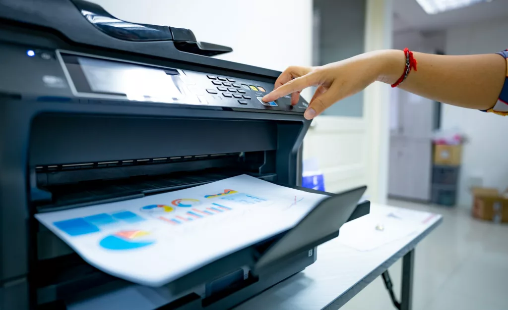Office worker prints paper on multifunction laser printer. Copy, print, scan, and fax machine. Image for e-faxing/digital fax pages of the Document Solutions section of the MCC website