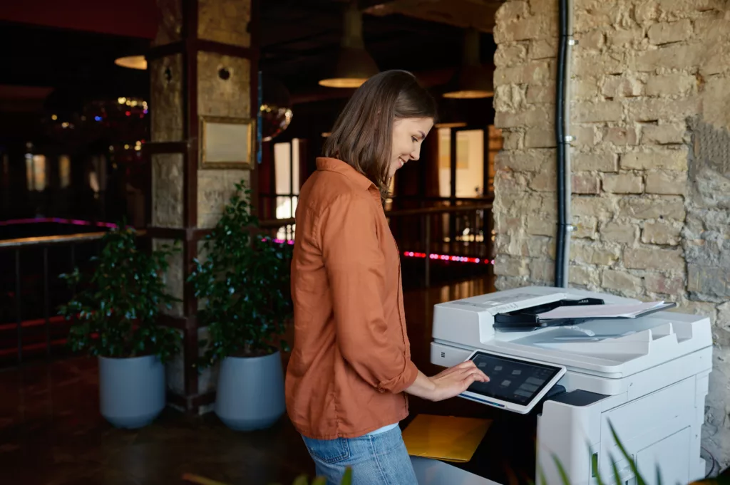 Young woman employee working on printer at coworking office - MCC Office Technology Solutions