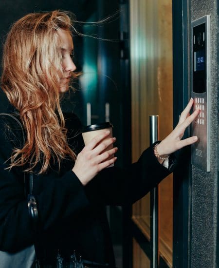 Woman dialing a number on the on video intercom at entrance of apartment building in the night